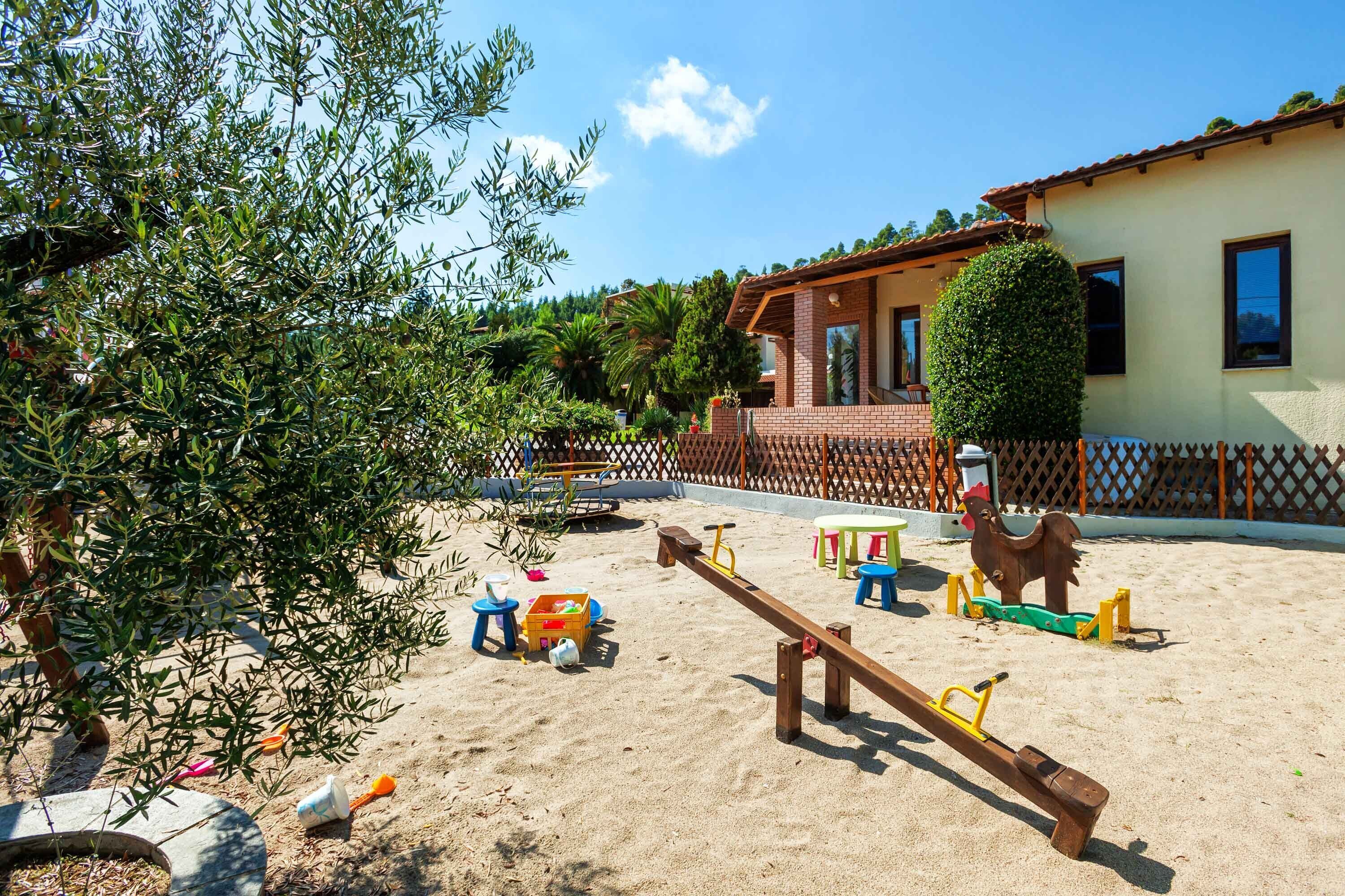 A sandy outdoor play area with seesaws and a fenced garden.