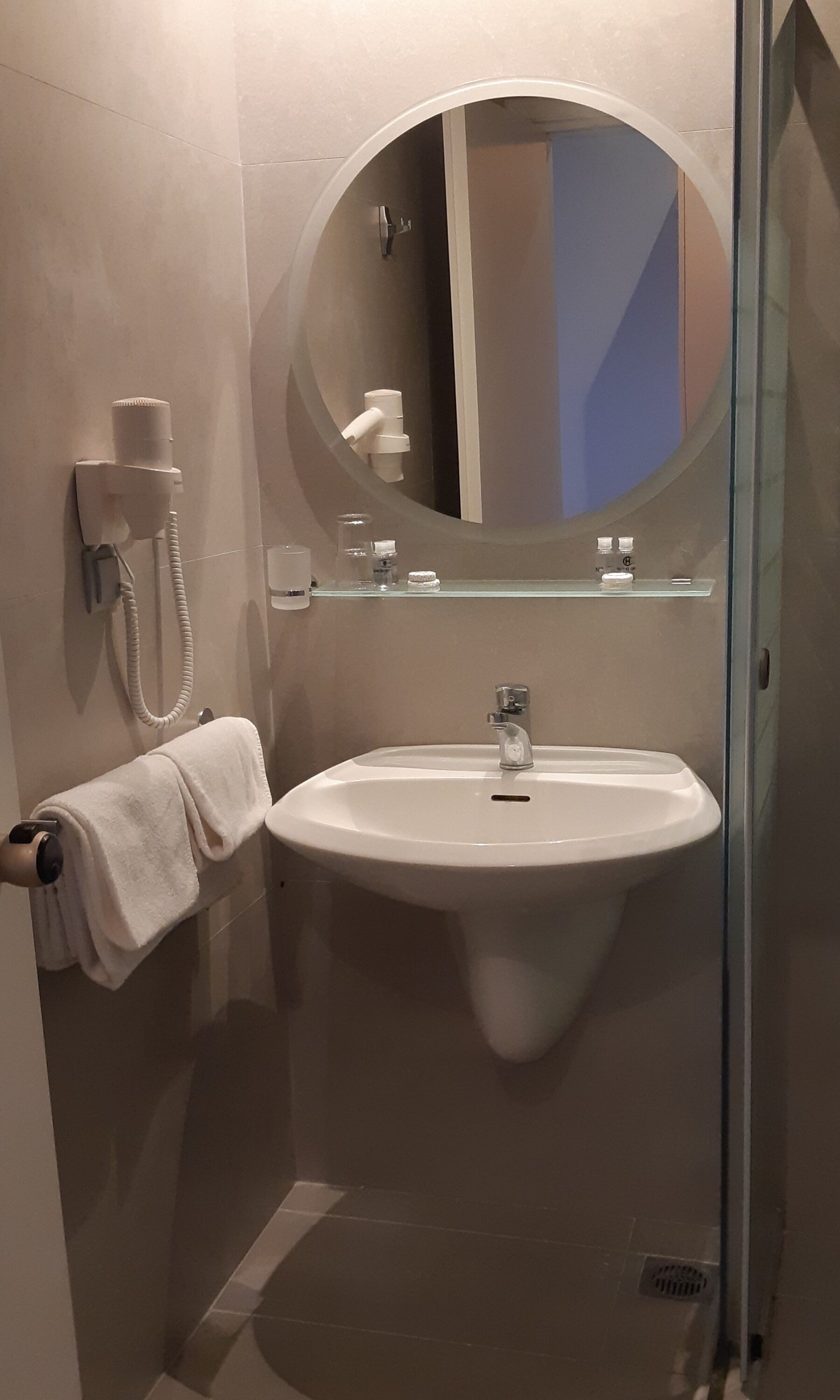 A modern bathroom with a white sink, a glass shower enclosure, a towel rack, and a mirror.