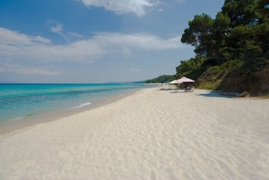 A beach with white sand, a clear blue sea, and a few umbrellas.