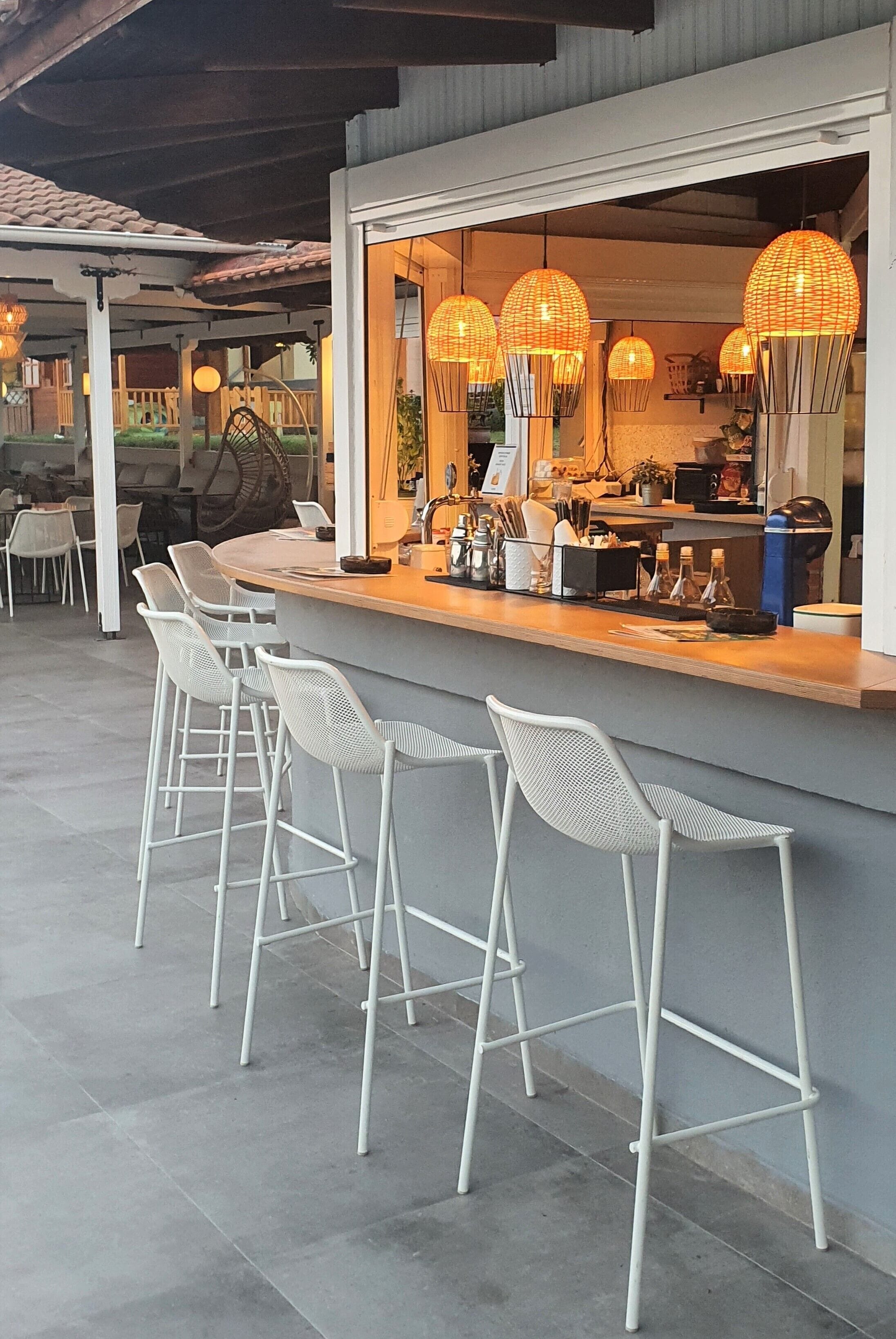 A bar area with white metal chairs, a counter with various items, and hanging spherical lights.