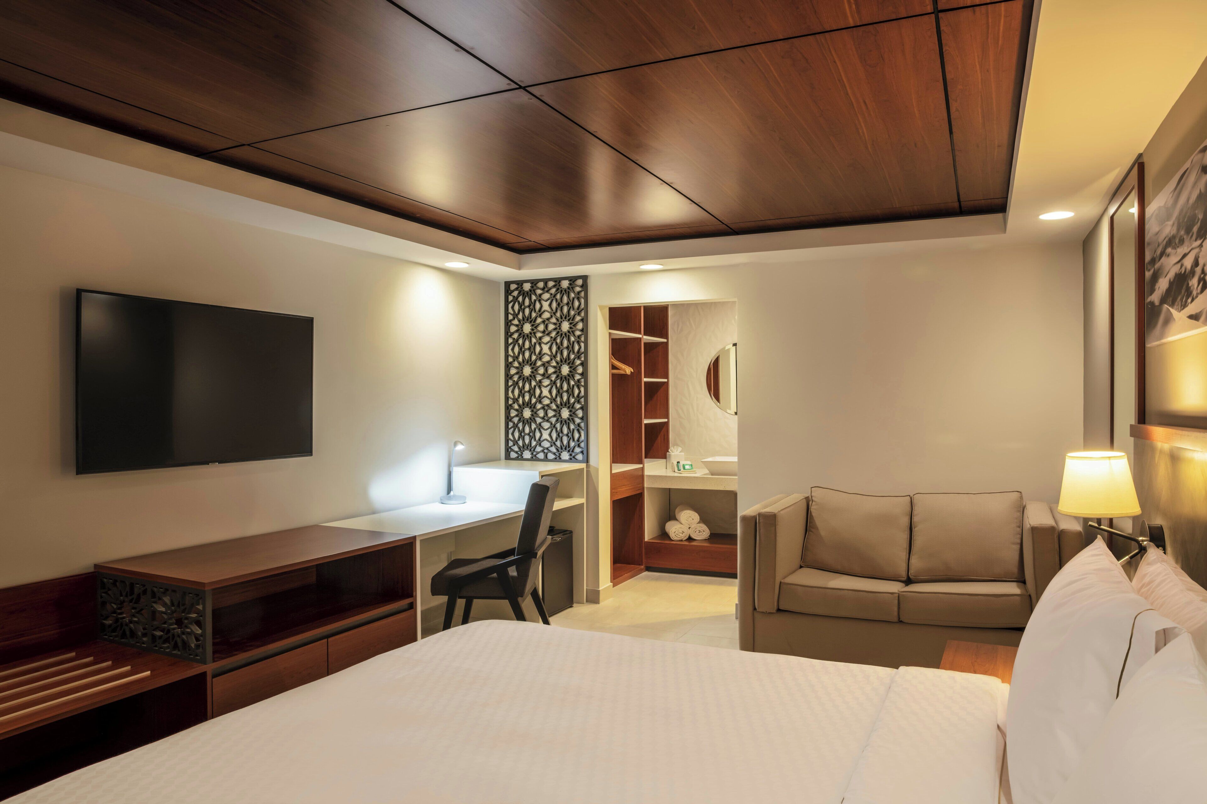 Une chambre d’hôtel moderne dotée d’un grand lit, d’un bureau, d’une chaise, d’un canapé, d’une télévision et d’un dressing.