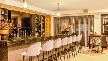 Una zona de bar con una barra larga, varios taburetes y una variedad de botellas y copas.