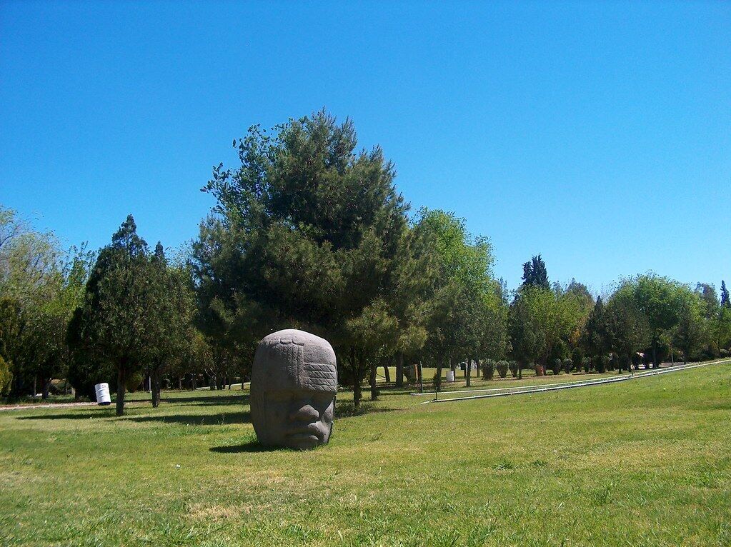 A large stone sculpture in a grassy park with trees in the background.