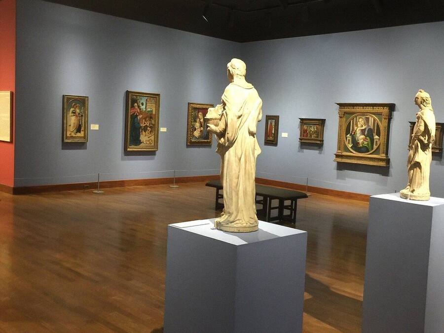 Uma galeria de arte com esculturas de mármore em pedestais, pinturas emolduradas nas paredes e soalho de madeira.