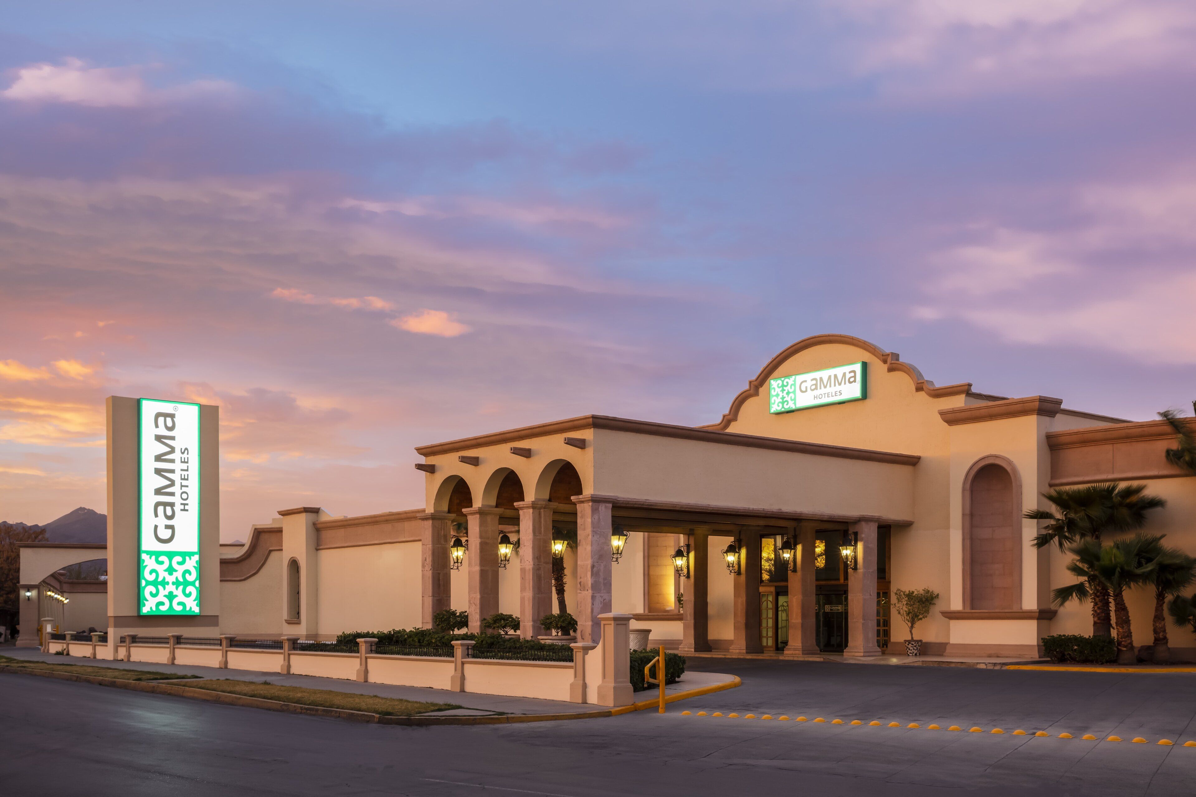 A hotel entrance with a sign, arched columns, and a landscaped area.
