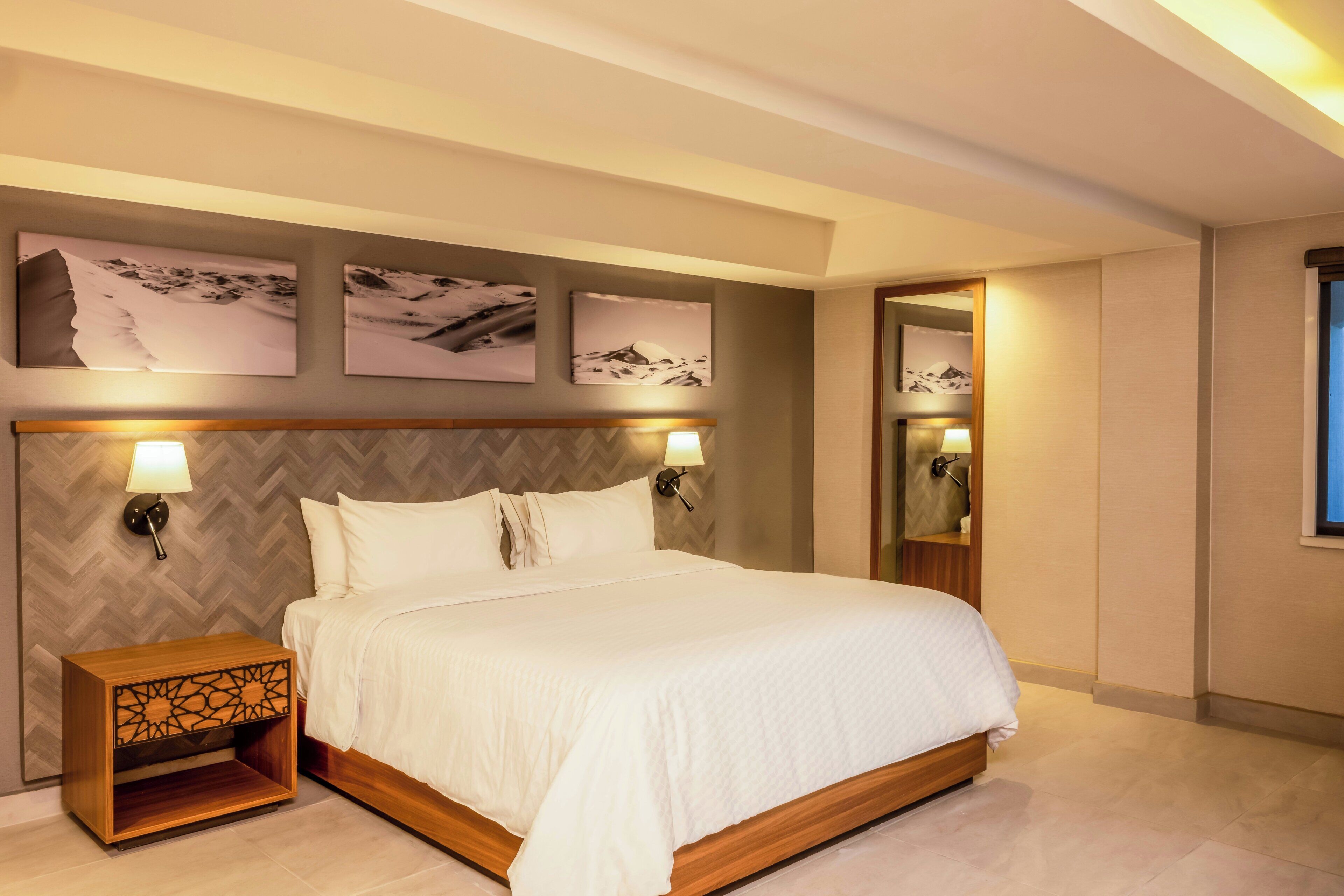 A neatly arranged hotel room with a large bed, two bedside lamps, and three wall-mounted pictures.
