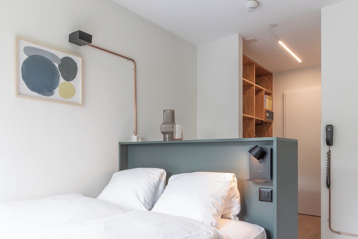 Ein modernes Hotelzimmer mit Bett, Nachttisch und einem Glas Wasser.