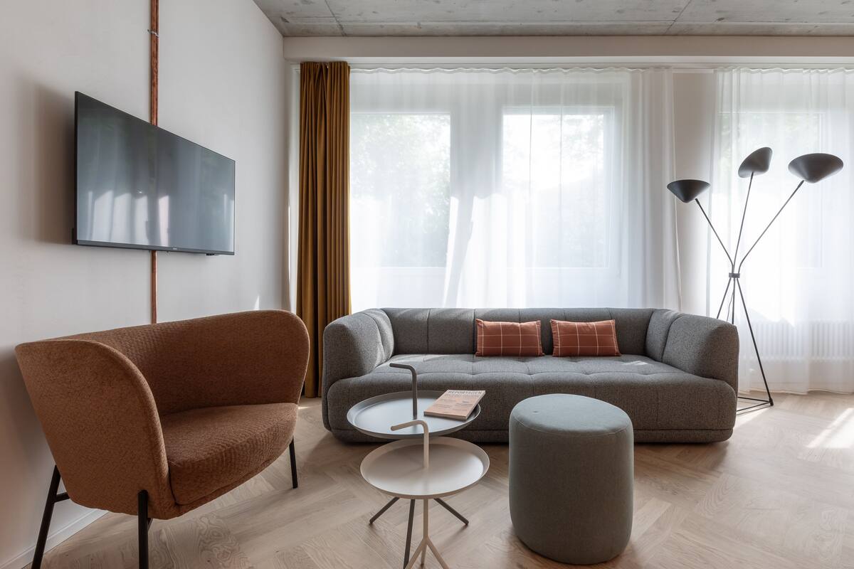 Ein modernes Wohnzimmer mit grauem Sofa, braunem Sessel, kleinem runden Tisch und einer Stehlampe.