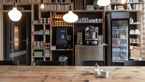 A cozy café with wooden shelves filled with books, a coffee machine, and a refrigerator stocked with beverages. - Alpenblick Bern (Bern)