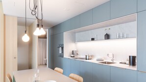 A modern kitchen with a white countertop, blue cabinets, and a built-in oven. There is a dining table with chairs and a vase with flowers on the counter. - Alpenblick Bern (Bern)