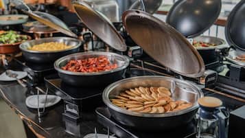 A buffet setup with various food items in bowls and pans, including pancakes and a dish that appears to be a type of casserole or salad.