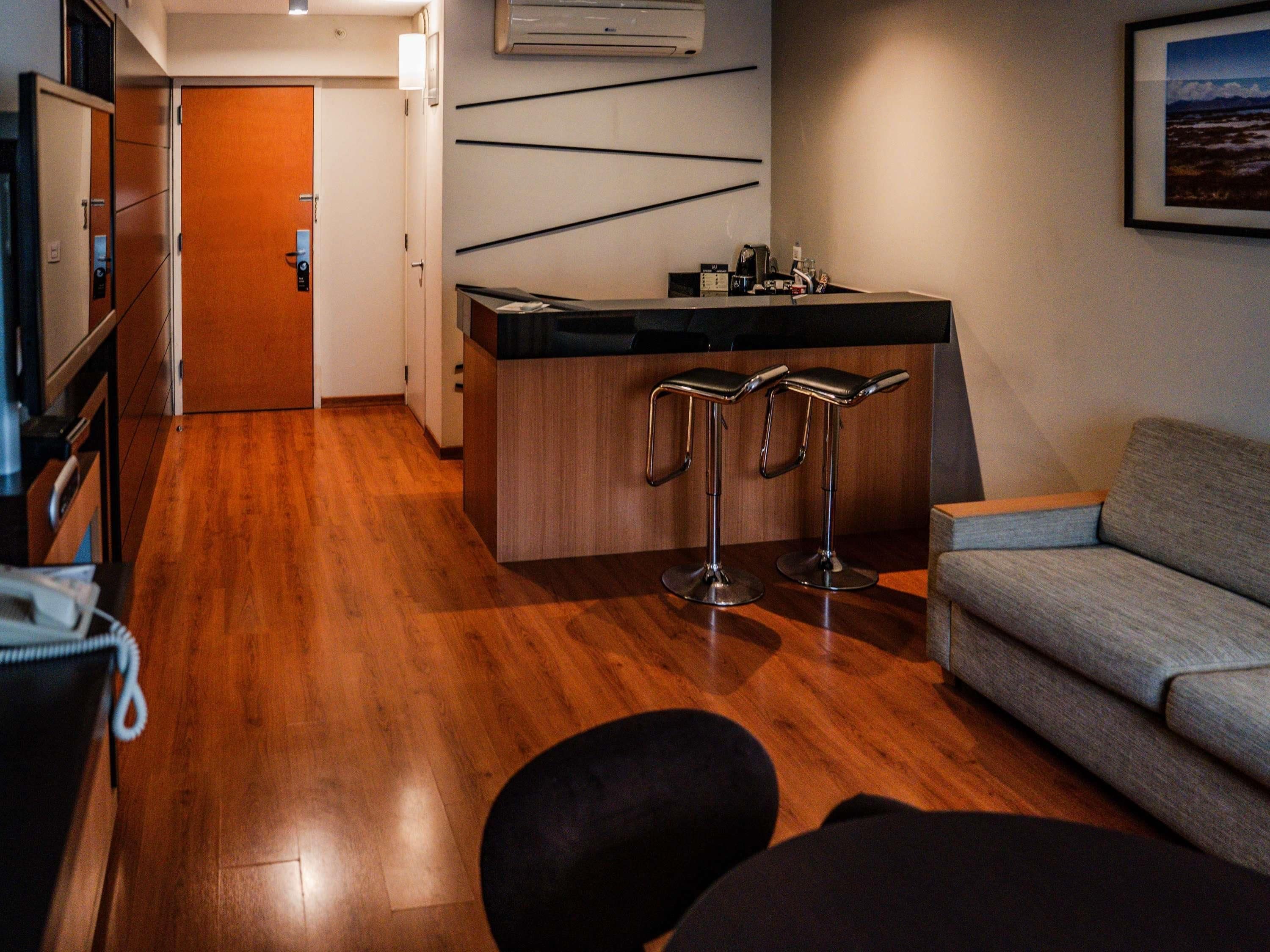 Una cocina moderna con suelo de madera, una zona de bar con taburetes, un sofá y un cuadro en la pared.