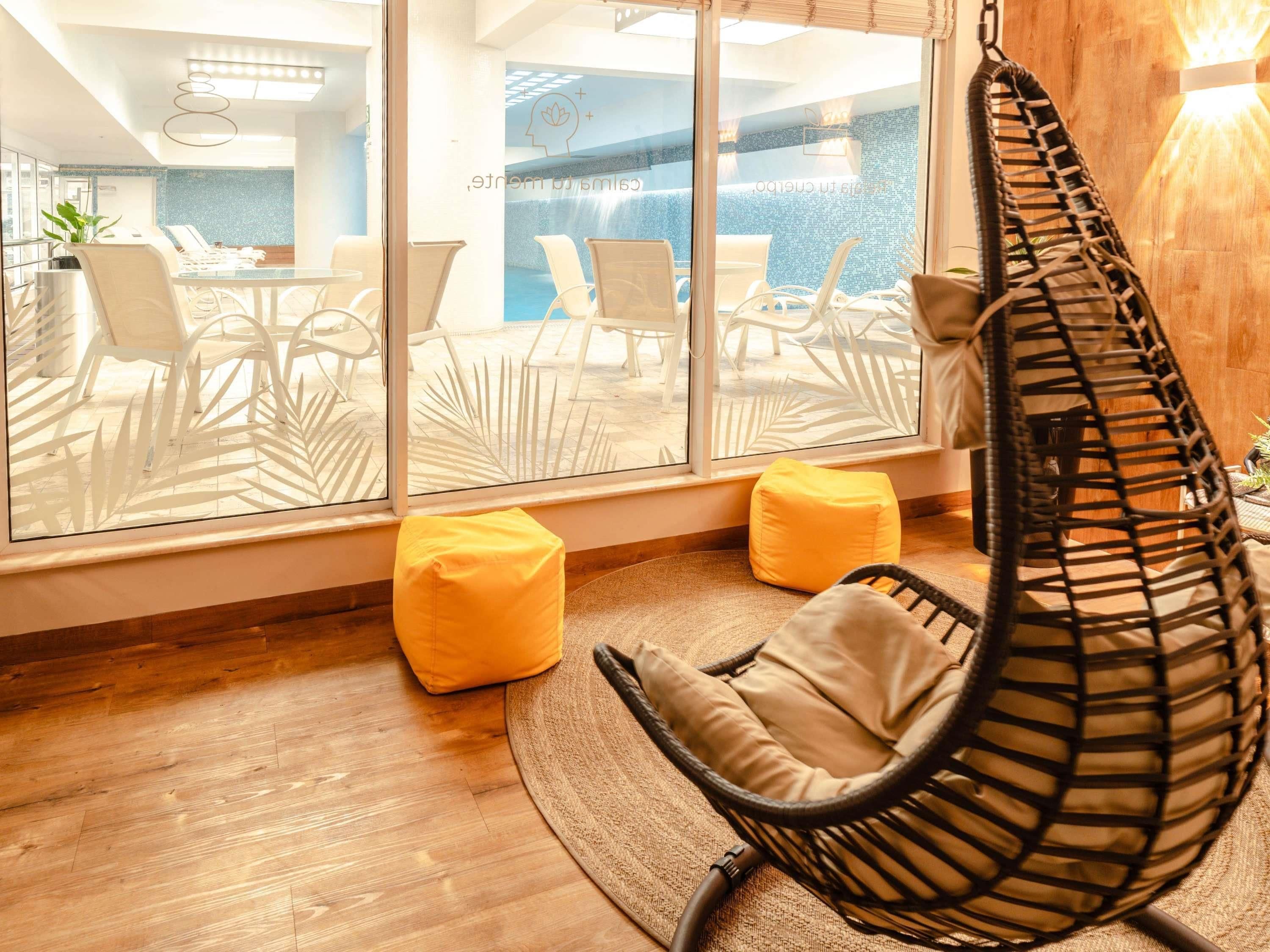 A modern room with a hanging chair, two yellow bean bags, and a view of an outdoor pool area through large windows.