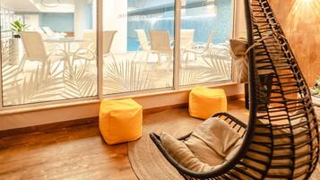 A modern room with a hanging chair, two yellow bean bags, and a view of an outdoor pool area through large windows.
