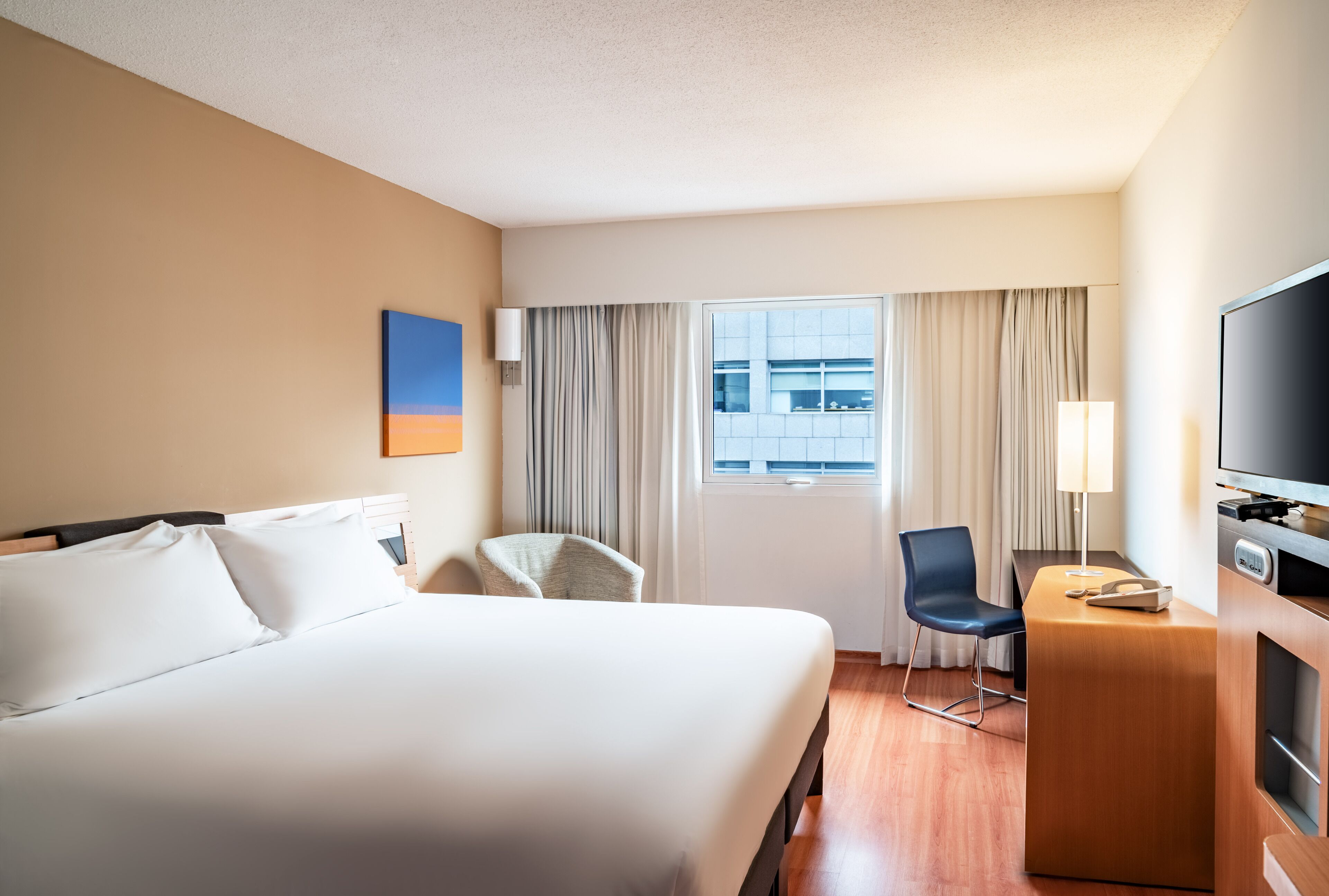 Una habitación de hotel con una cama grande, un escritorio con televisor y una silla.