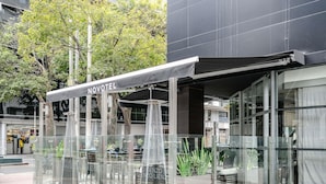 A modern hotel with a glass facade, outdoor seating area, and a sign reading "NOVOTEL".