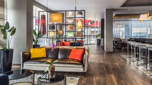 A modern hotel lobby with a leather sofa, a coffee table, and a glass-top table. There is a large window with a view of the outside.