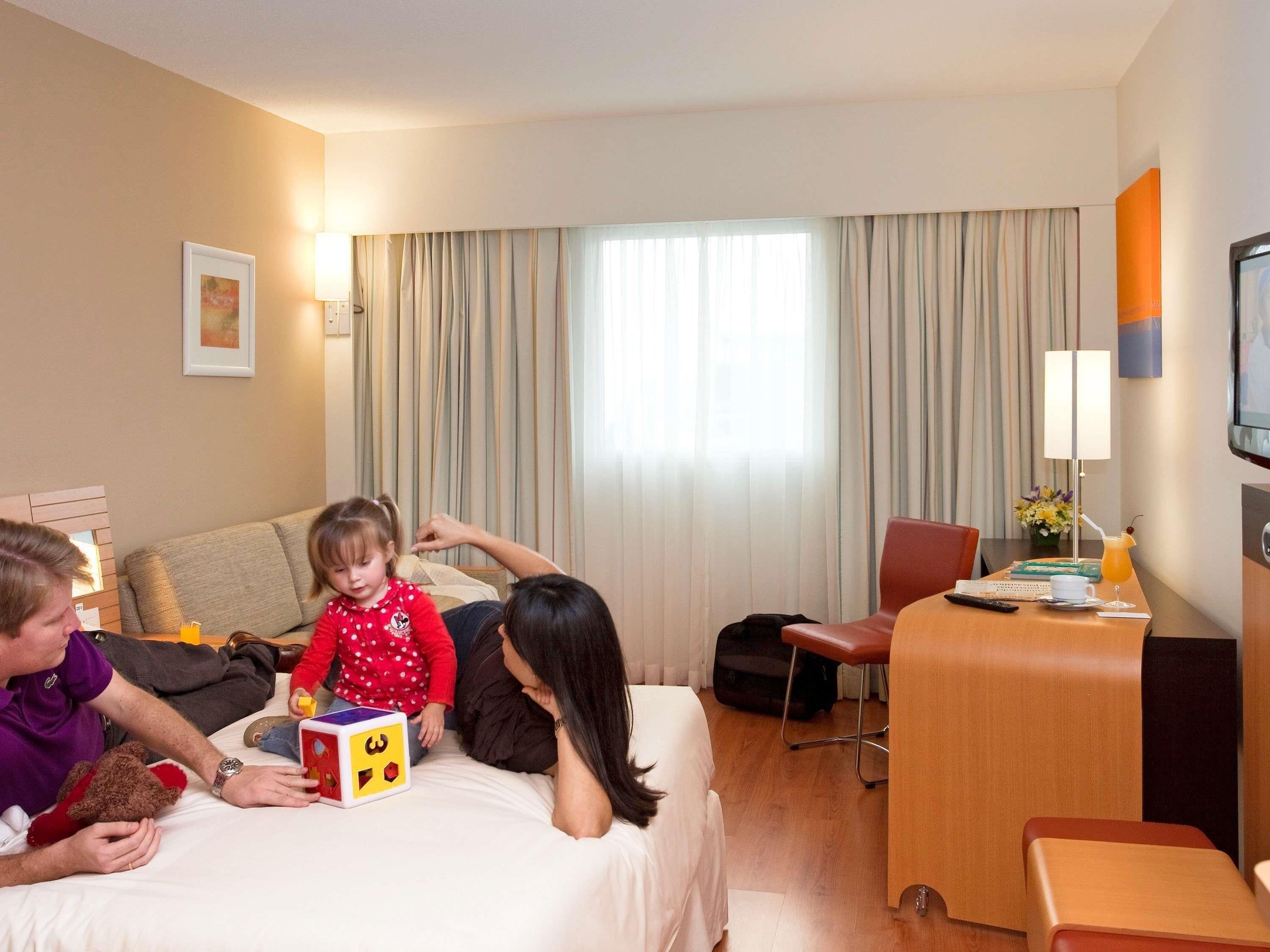 A hotel room with a bed, a desk, a TV, and a window with curtains.