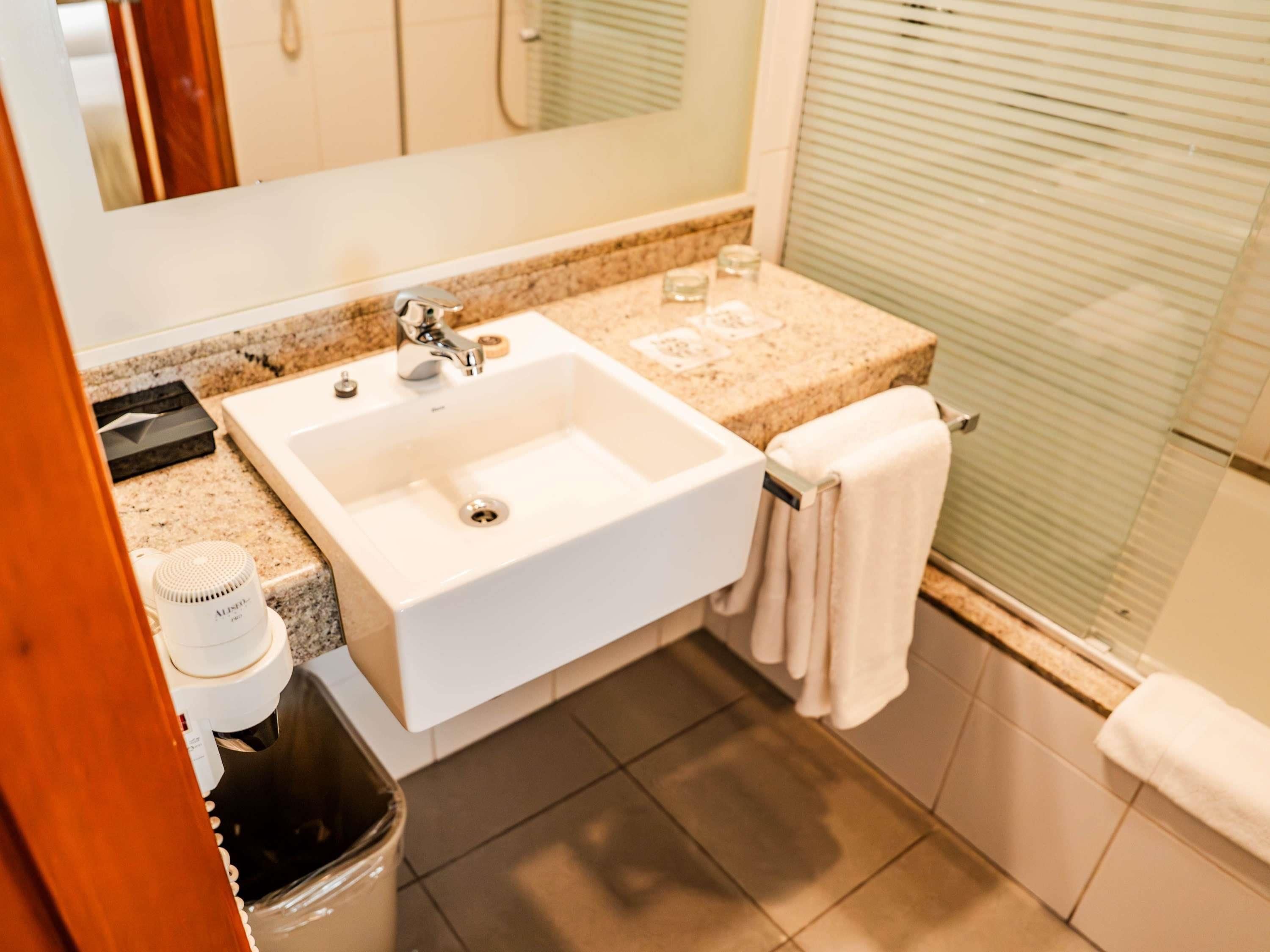 Un baño con lavamanos blanco, espejo, toallero y zona de ducha.