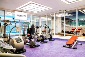 A Novotel gym with various exercise equipment, a purple floor, and a sign indicating the exit.