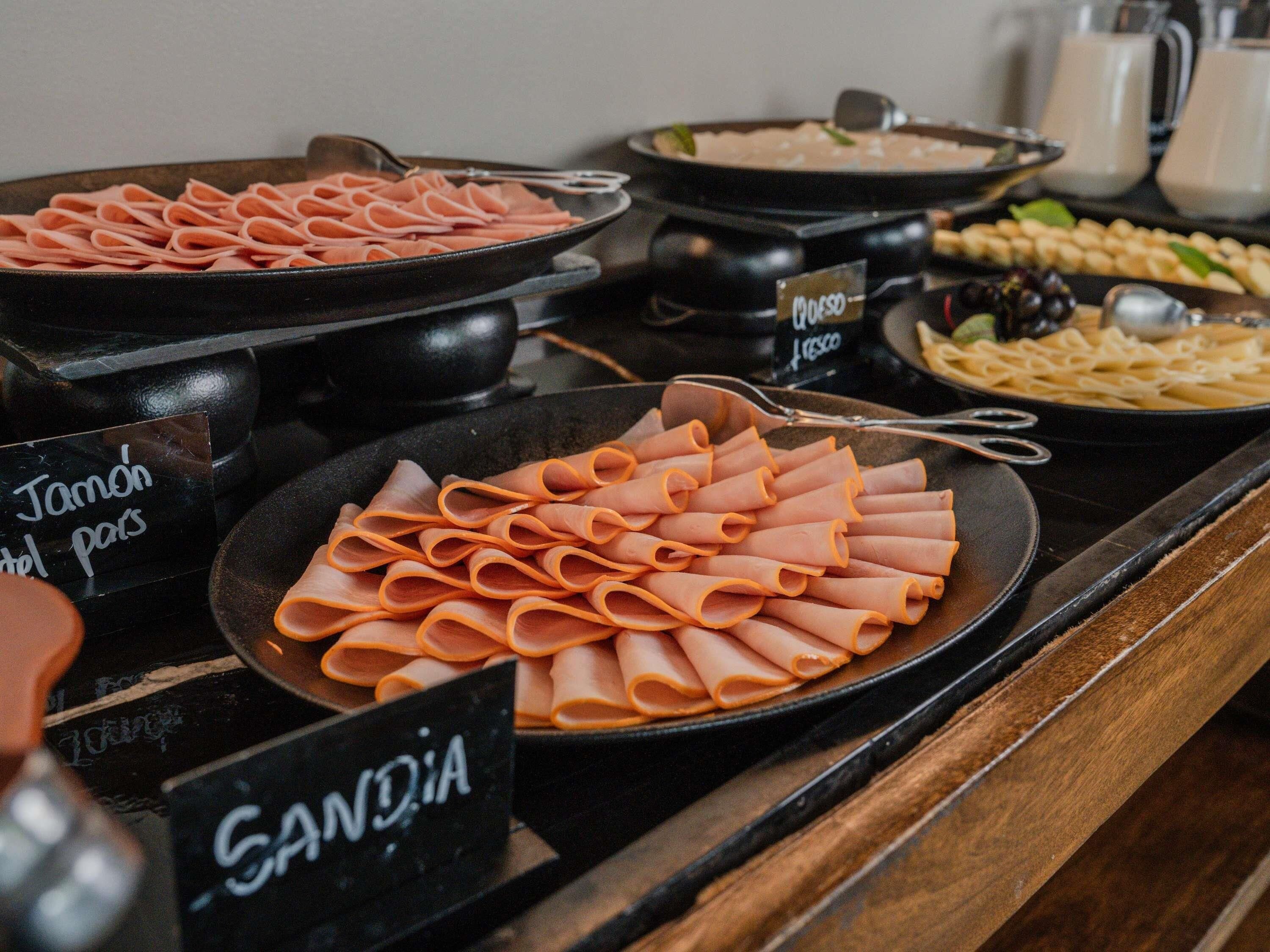 Un bufé con diversas opciones de comida, incluyendo jamón, pasta y otros platos.