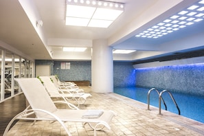 A swimming pool area with lounge chairs and a tiled floor.