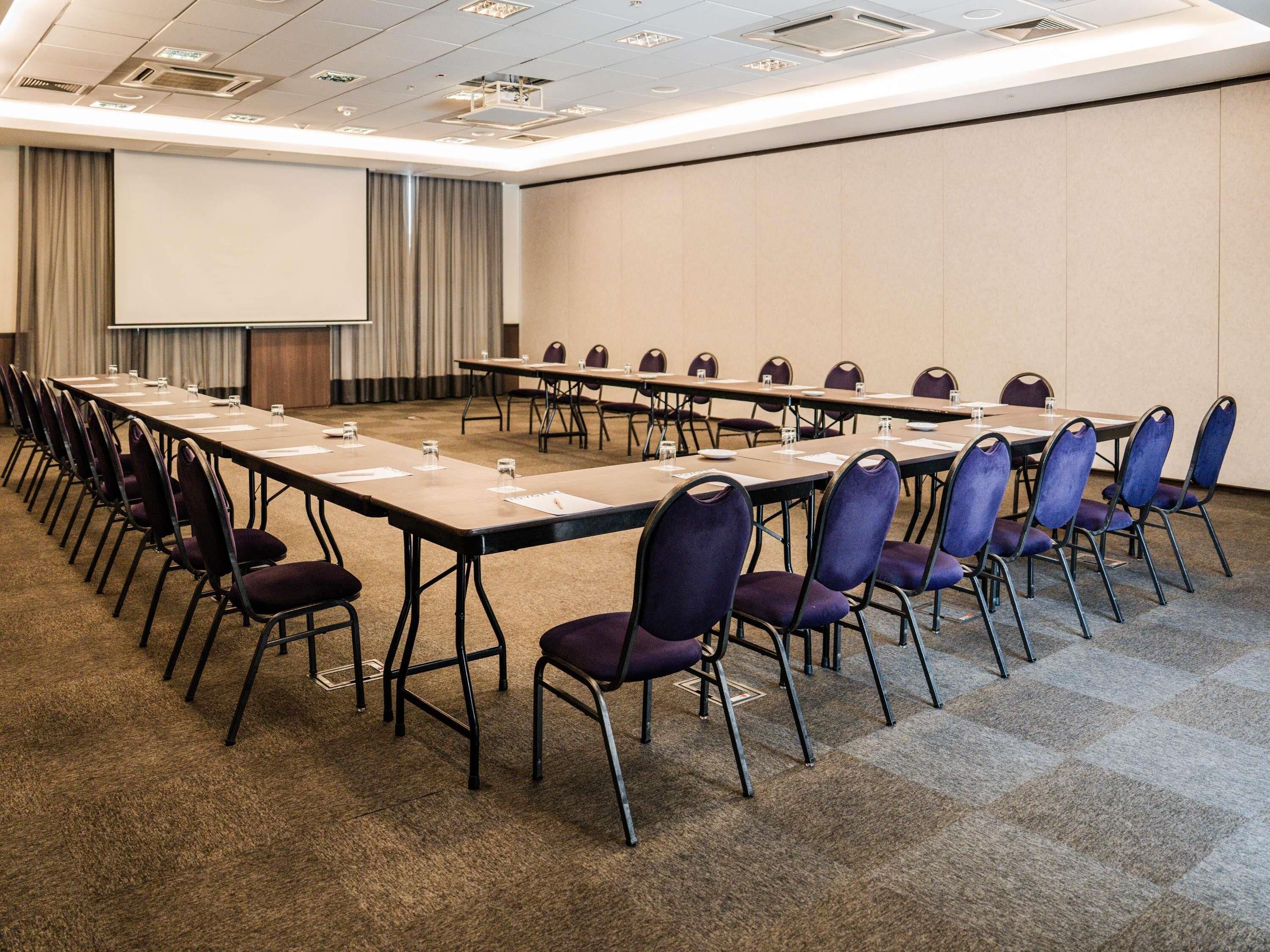 Une salle de conférence avec une longue table, des chaises, un écran de projection et un sol recouvert de moquette.