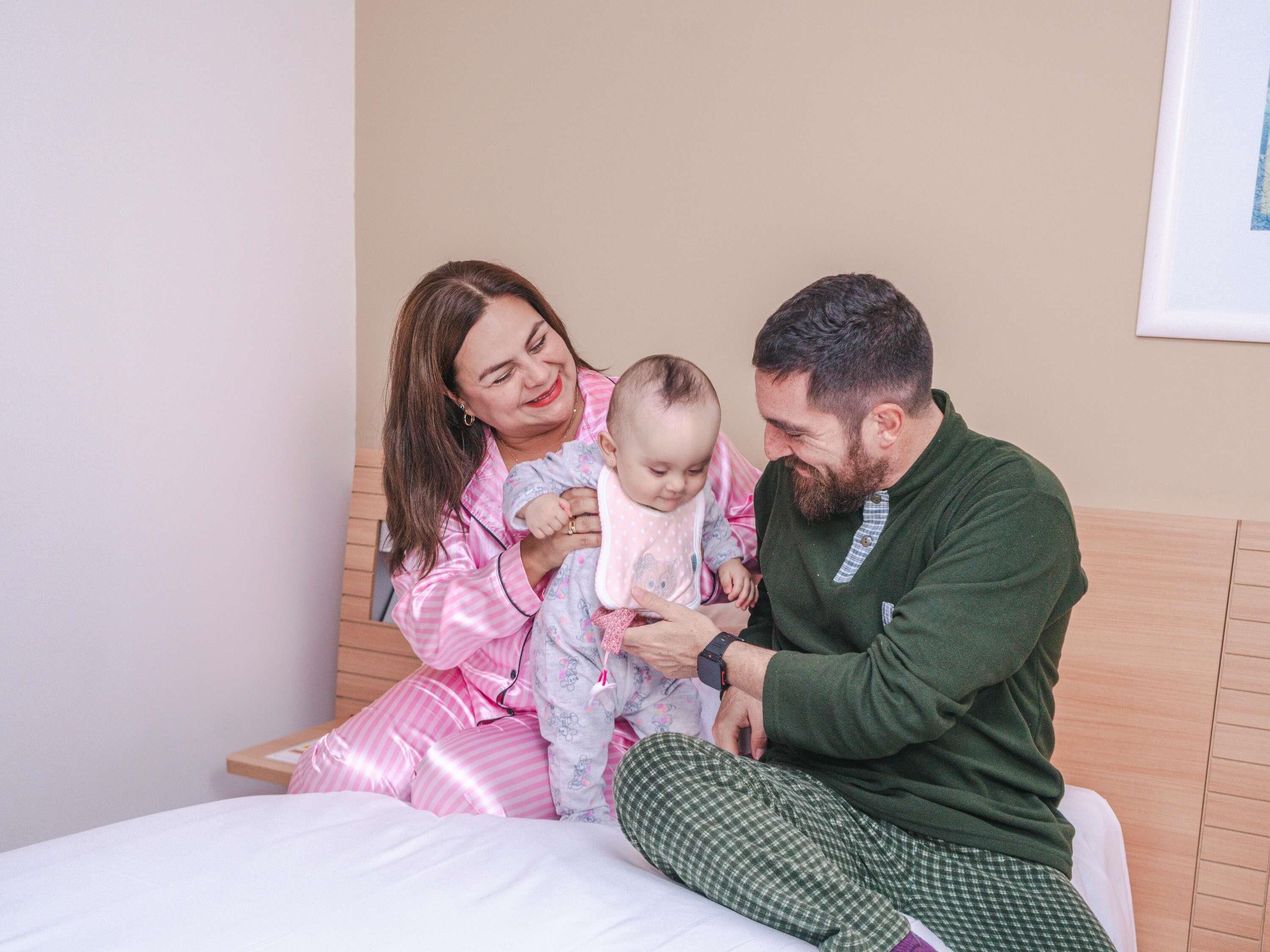 A family on a bed with a wooden headboard, a plain wall, and a framed picture.