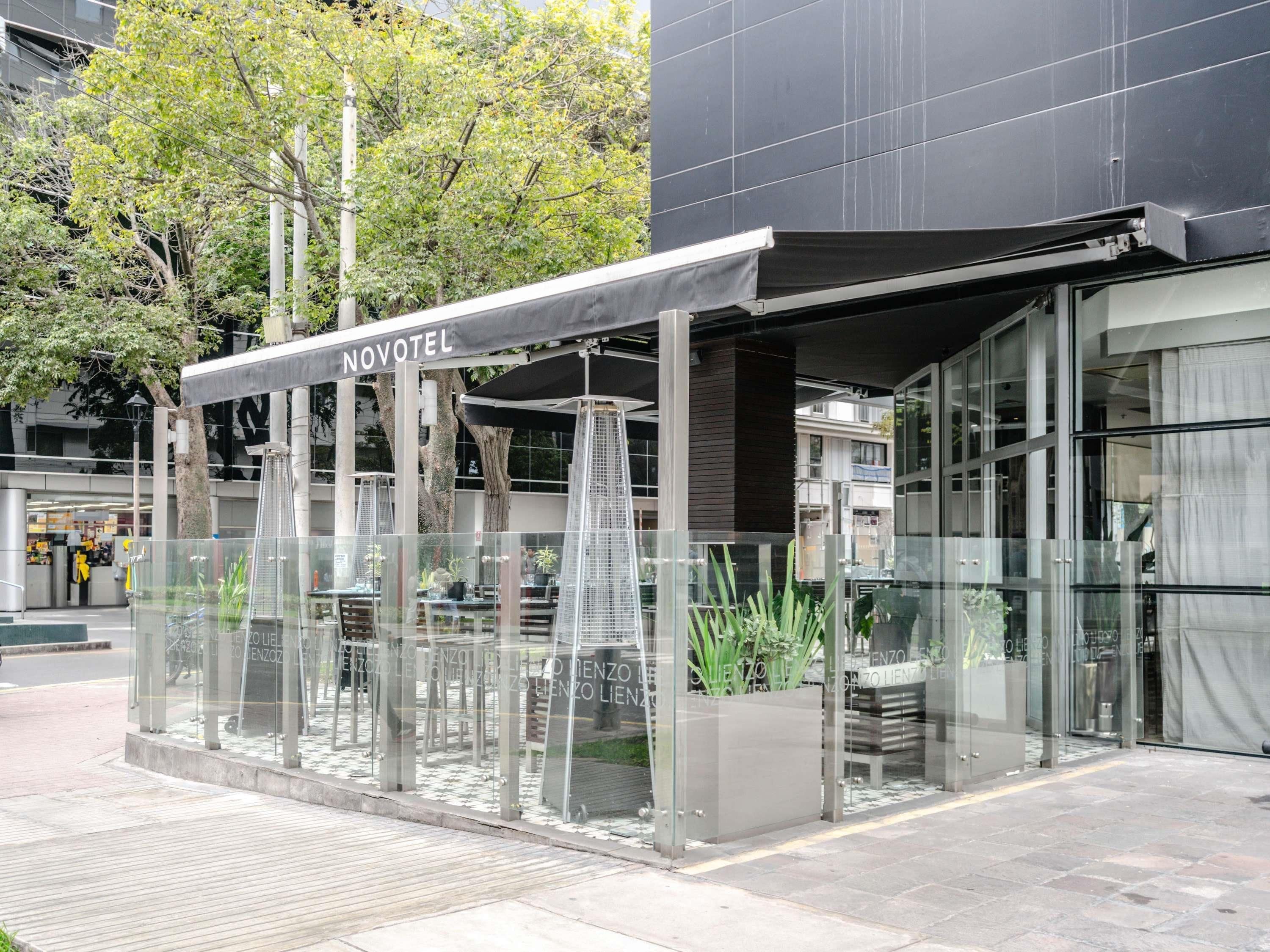 A modern hotel with a glass facade, outdoor seating area, and a sign reading "NOVOTEL".