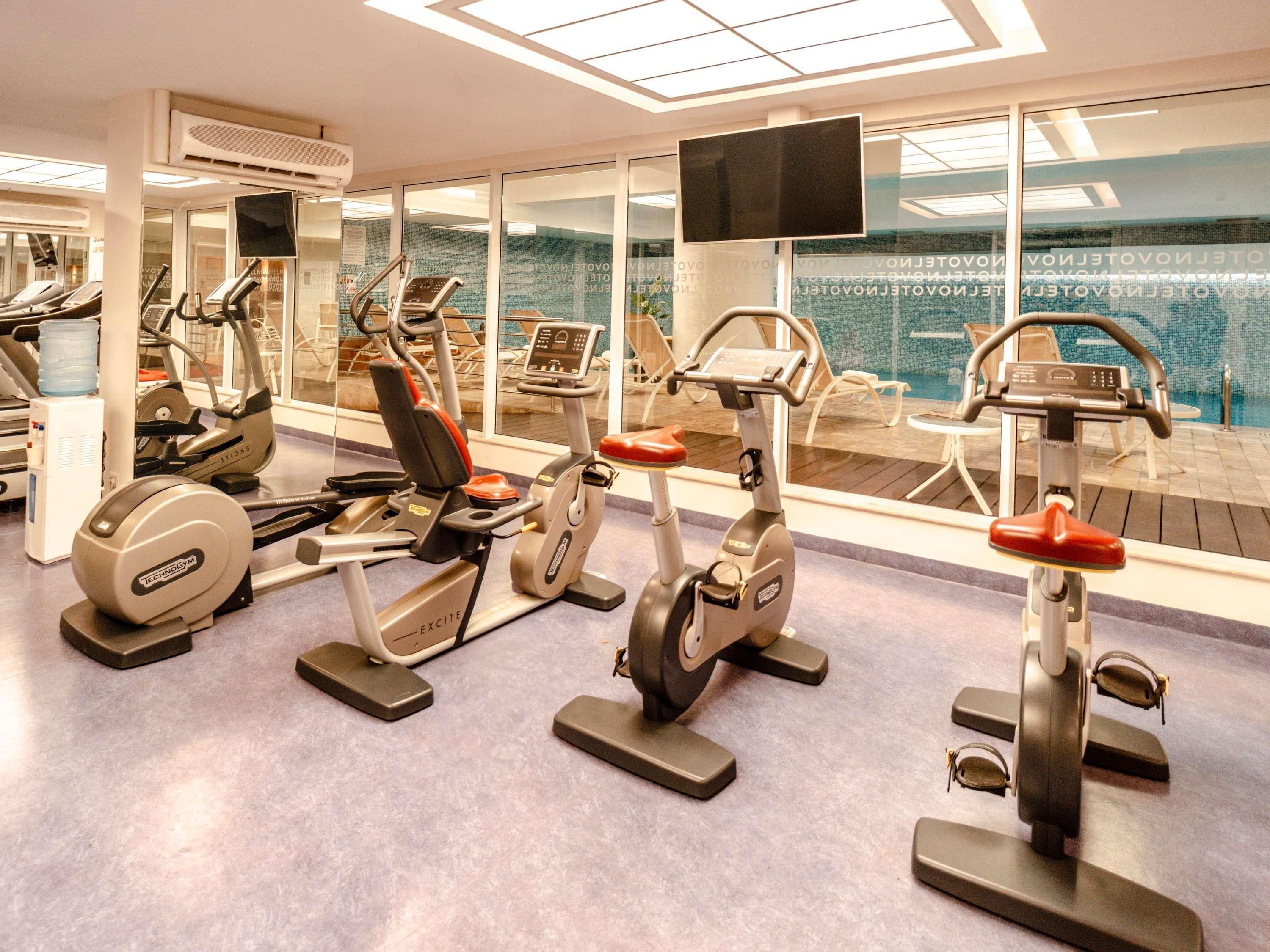 Un gimnasio con diversas máquinas de ejercicio, un dispensador de agua y un amplio ventanal con vistas.