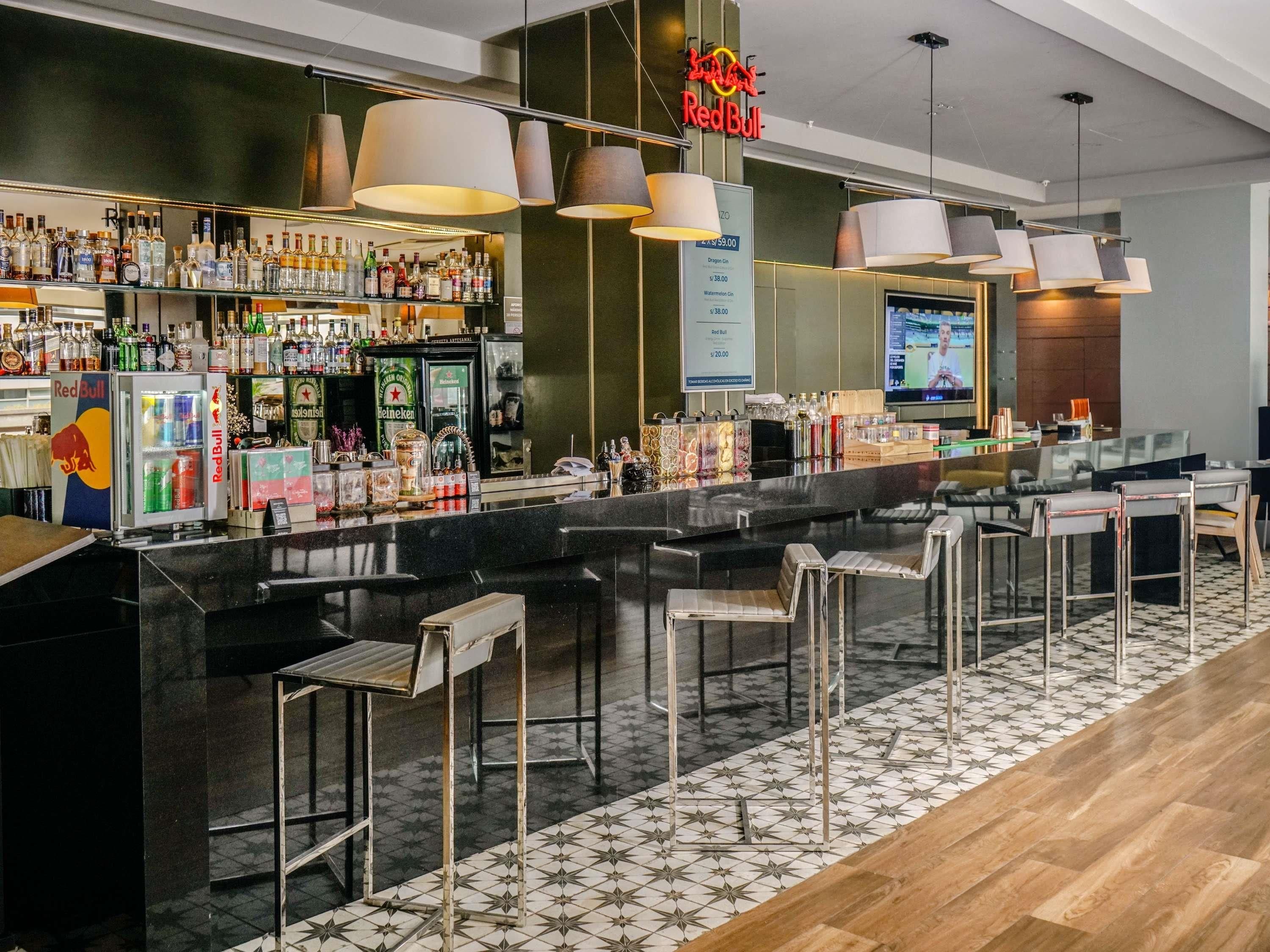 A modern bar area with a variety of liquor bottles, a Red Bull refrigerator, and a television screen.