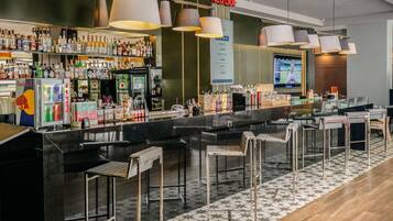 Uma área de bar moderna com diversos tipos de bebidas alcoólicas, um refrigerador de Red Bull e uma tela de televisão.