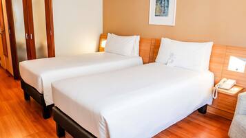 A hotel room with two beds, wooden flooring, a wooden headboard, a bedside table with a phone, and a framed artwork on the wall.