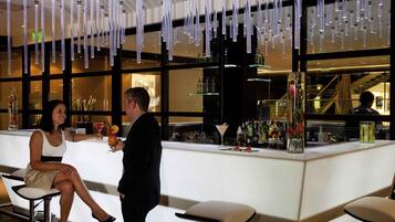 A bar area with hanging light fixtures, a counter with various bottles, and a seating area with stools.