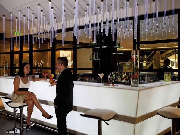 Una zona de bar con lámparas colgantes, una barra con diferentes botellas y un área de asientos con taburetes.