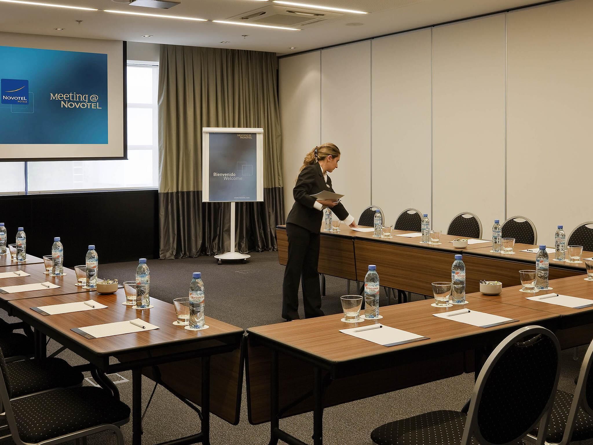 A meeting room with a long table, chairs, water bottles, and a presentation screen.