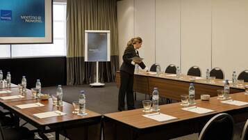 A meeting room with a long table, chairs, water bottles, and a presentation screen.