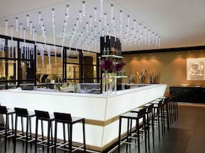 A modern bar area with a central island, black bar stools, hanging pendant lights, and a large window. - Novotel Buenos Aires (Buenos Aires)