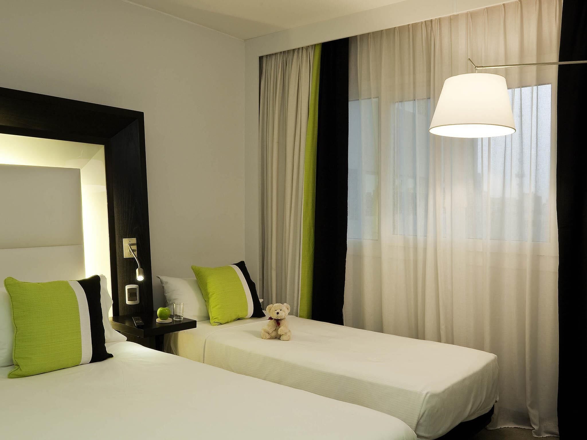 Een hotelkamer met twee bedden, een nachtkastje, een lamp en een teddybeer.