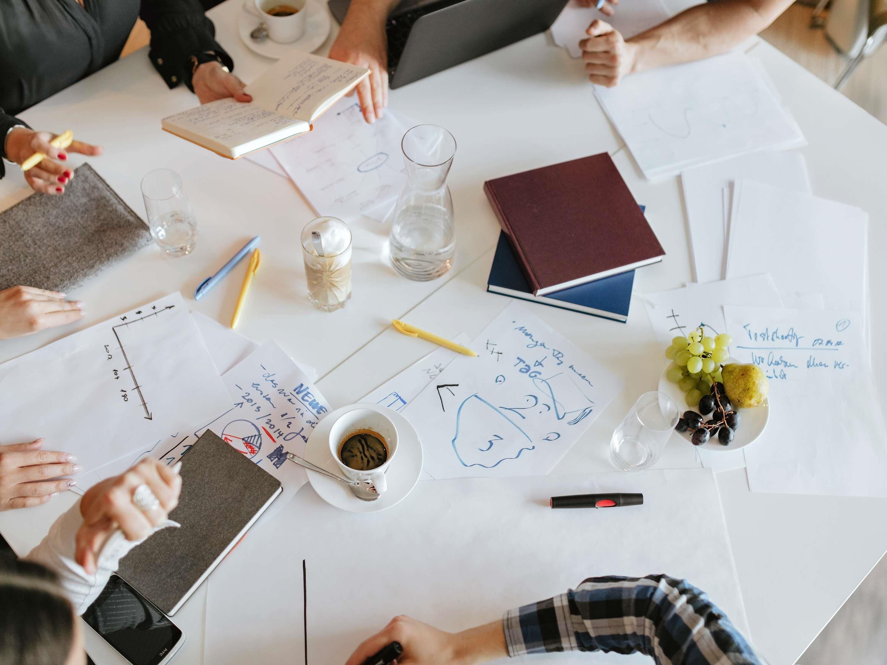 A group of people at a table with documents, a laptop, a coffee cup, and a glass of water.