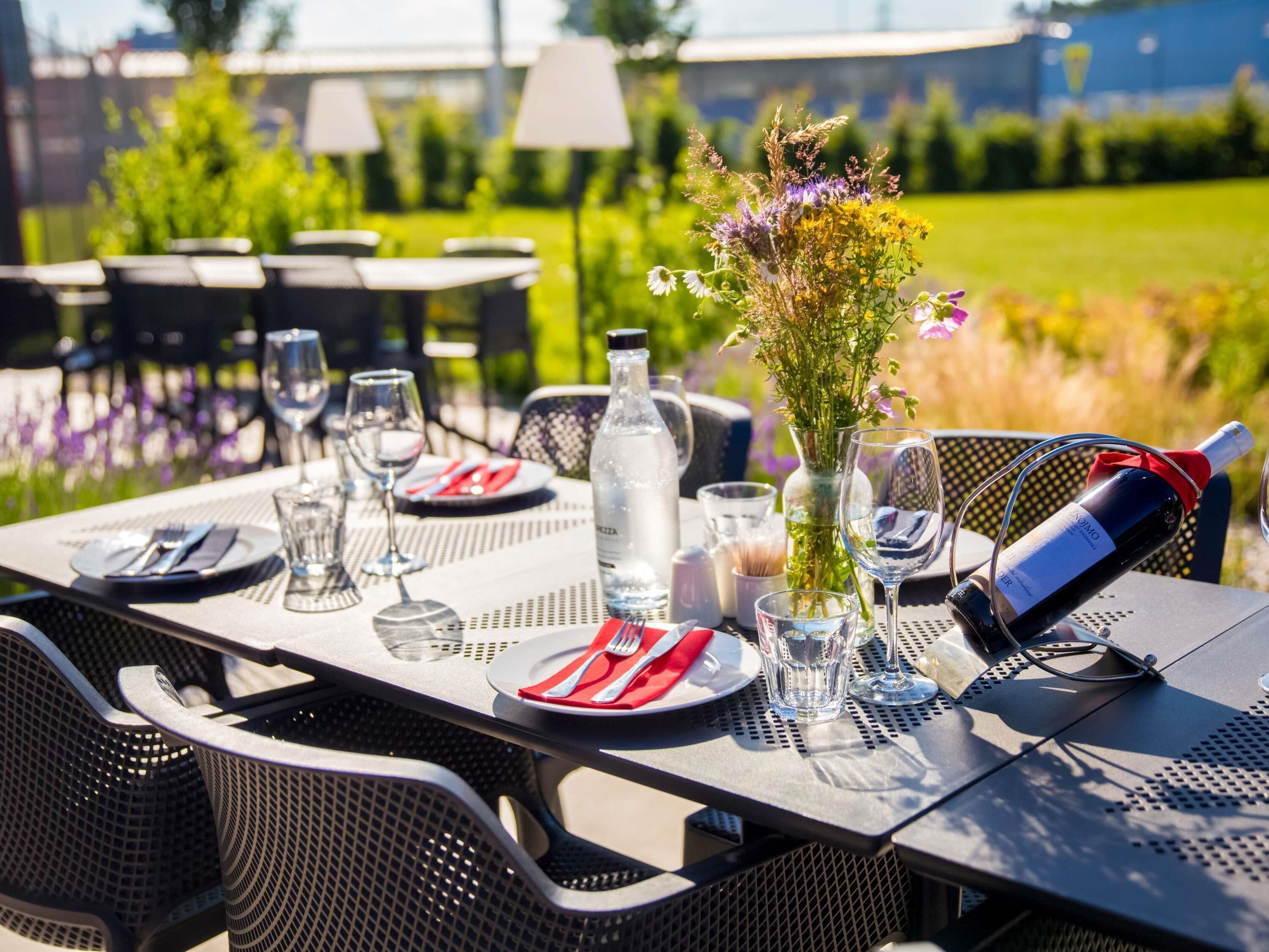 An outdoor dining table set with plates, cutlery, glasses, a water bottle, and a wine bottle.