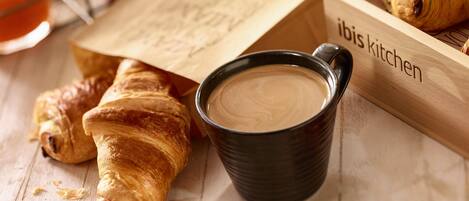 A wooden tray with croissants and a cup of coffee, and a paper bag with text.