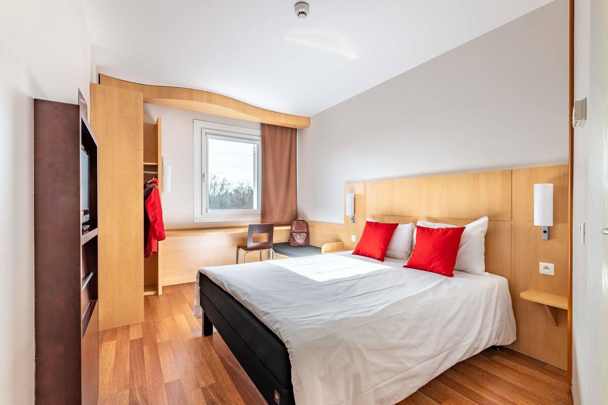 Ein Hotelzimmer mit einem Bett, einem Schreibtisch, einem Stuhl, einem Fenster und einem Kleiderschrank.