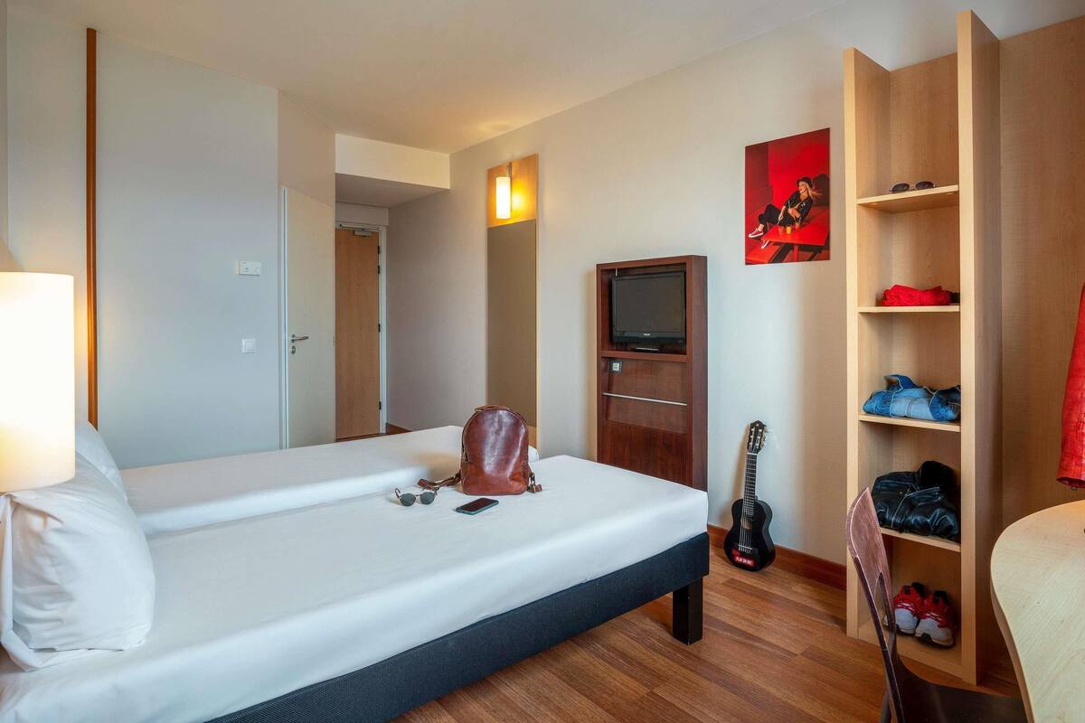 Ein Hotelzimmer mit einem Bett, einem Fernseher, einer Gitarre, einem Sessel und einem Schuhregal.