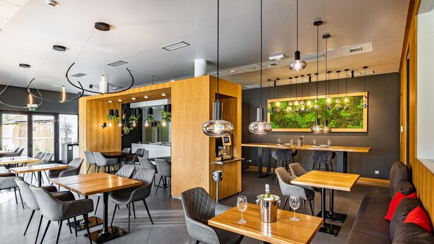 A modern restaurant interior with wooden tables, grey upholstered chairs, and pendant lighting. - ibis Plzen (Plzen)