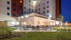 A hotel with multiple floors, outdoor seating area, and a well-lit entrance. - ibis Plzen (Plzen)