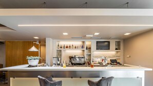 A modern bar area with a long counter, two bar stools, a coffee machine, and a TV mounted on the wall. - ibis Plzen (Plzen)