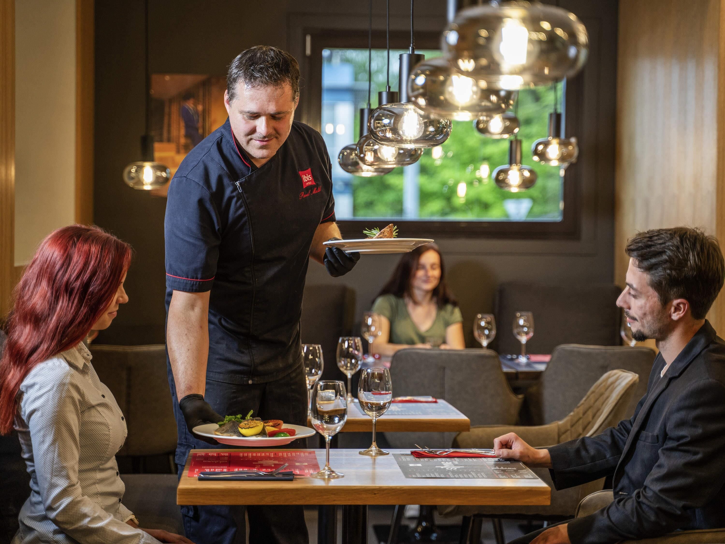 A restaurant interior with a waiter serving a dish to a table.