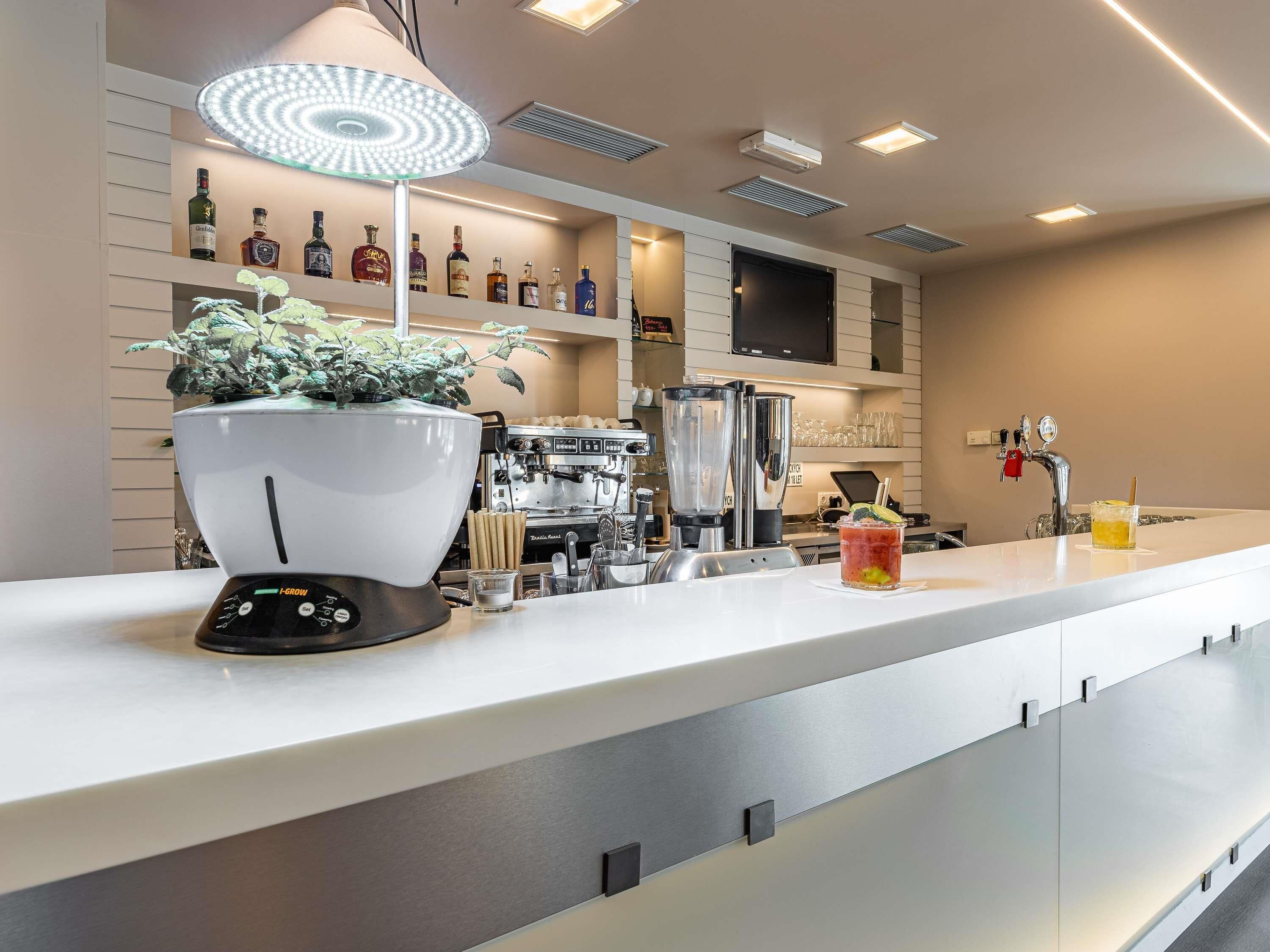 A modern bar area with a coffee machine, a large planter with green plants, and a variety of liquor bottles on shelves.
