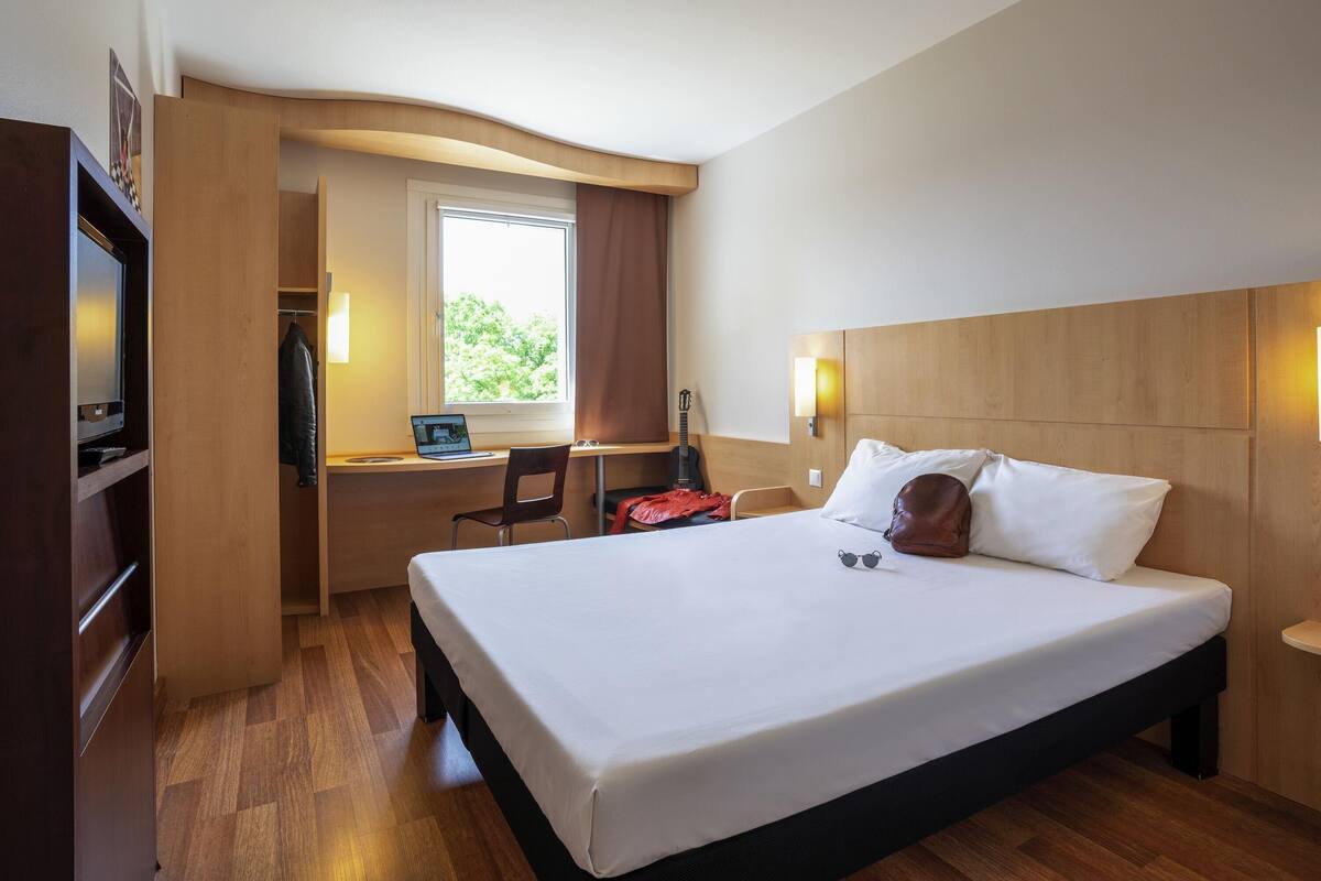 Una habitación de hotel con cama, escritorio, laptop, guitarra y televisión.
